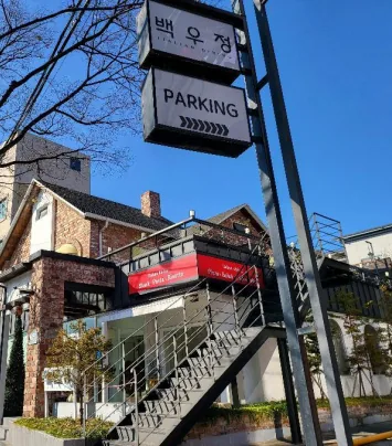 맑은 날의 벽돌 건물 외관 — 기둥 간판 «백우정 ITALIAN DINING»·«PARKING», 2층으로 오르는 철제 계단, 빨간 차양